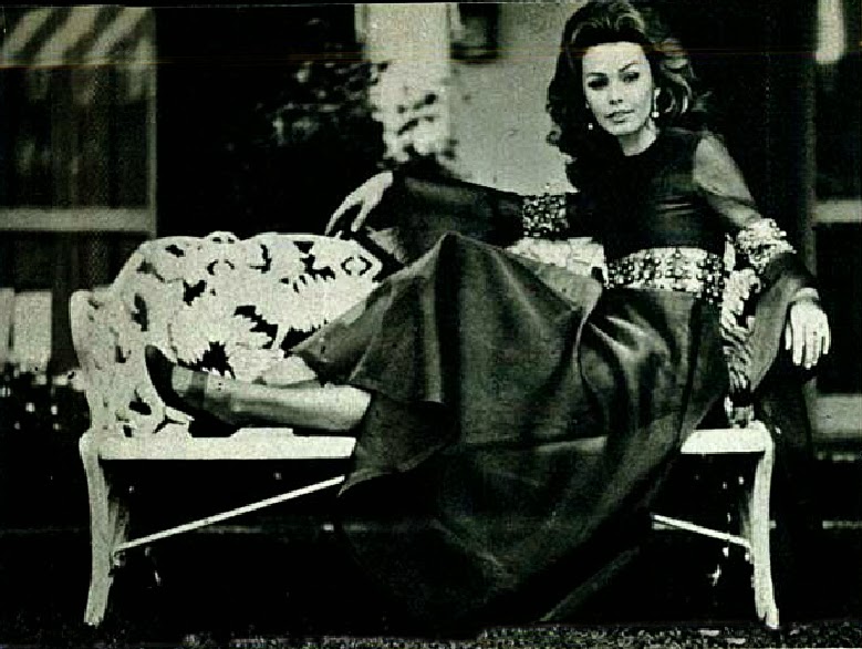 Foto da atriz Ângela Diniz, foto em preto e branco de uma mulher com vestido preto sentada em uma banco de ferro branco. Fim da descrição